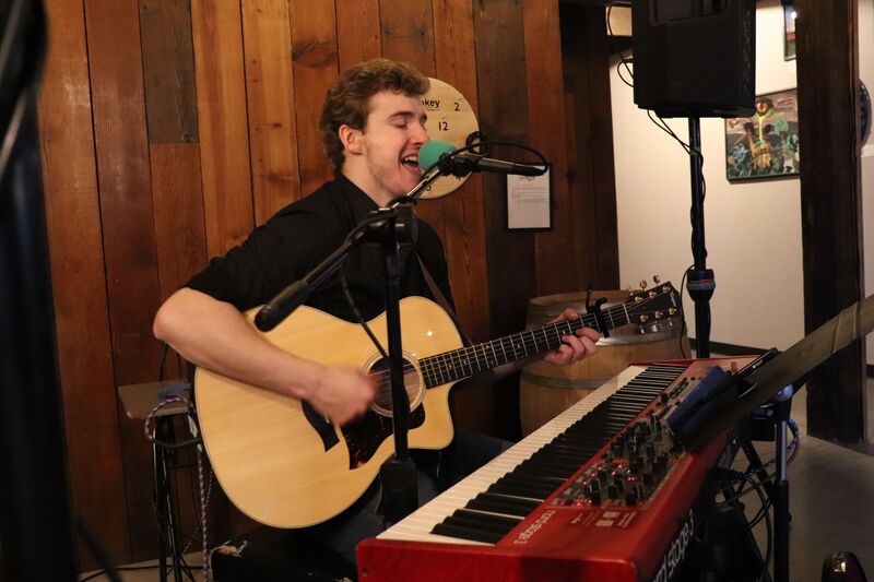 Ryan Howe performing with guitar and red keyboard at a rustic indoor venue