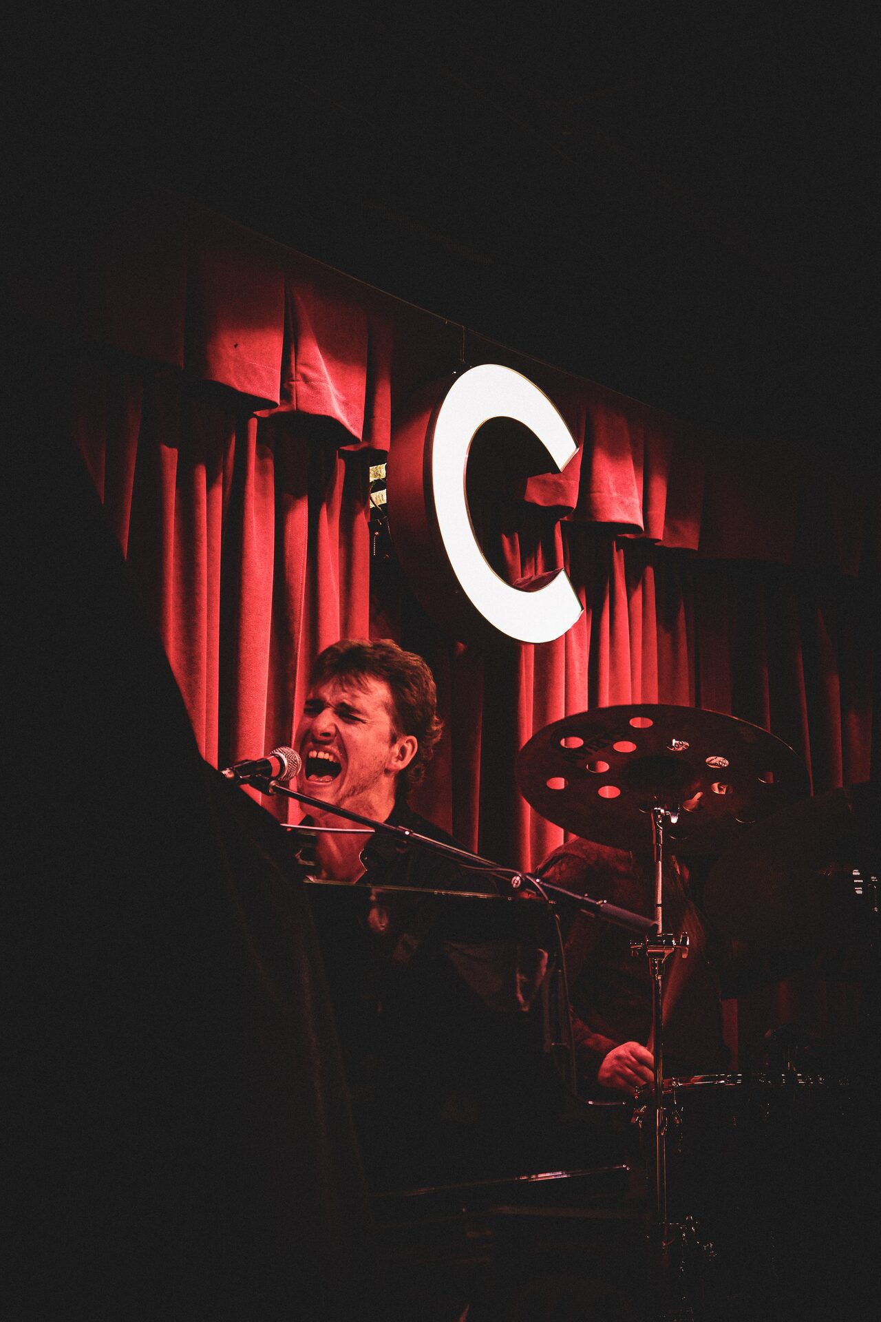 Ryan Howe performing on a dramatically lit nightclub stage with red curtains