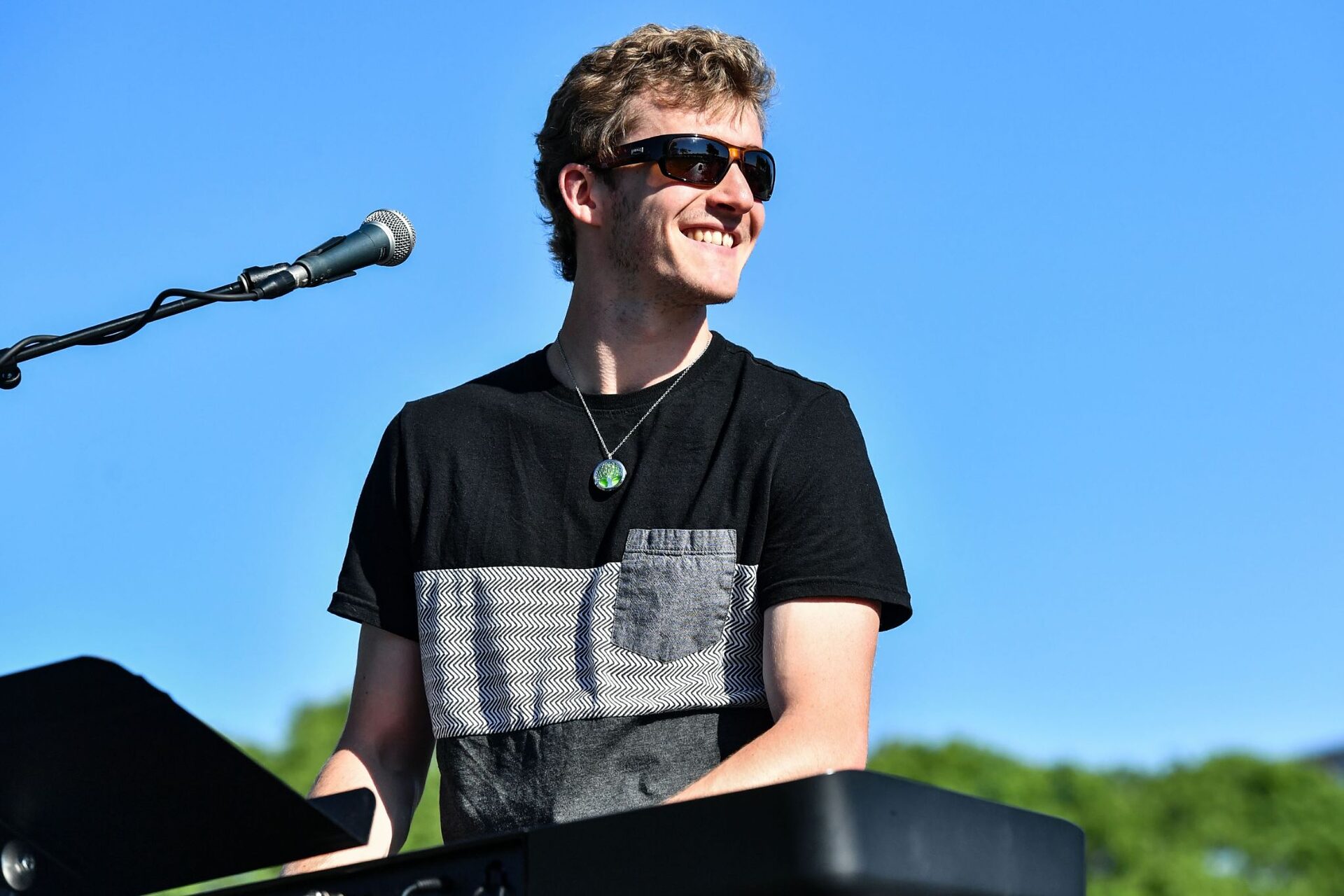 Ryan Howe smiling at keyboard on an outdoor stage under blue sky